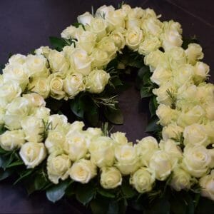 Photo of a funeral tribute, a white rose open heart with foliage collar. White roses arranged en masse