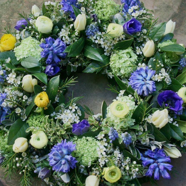 Photo showing a sample funeral wreath tribute in blue, lemon and white spring flowers from Kensington flowers