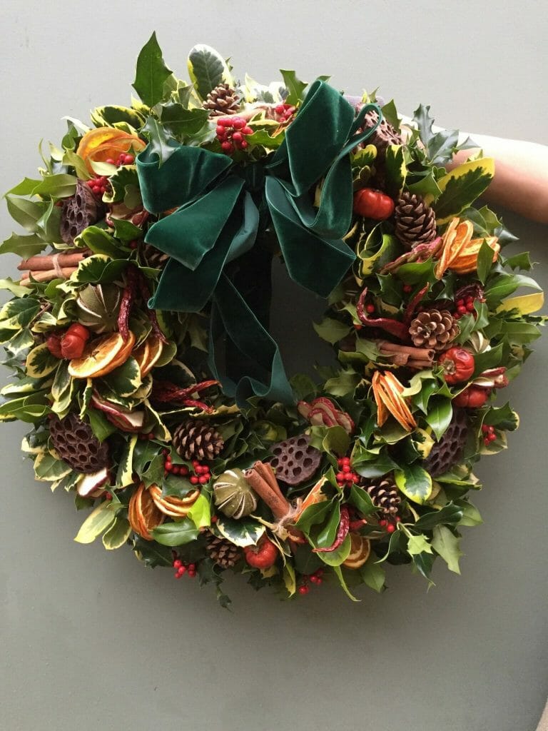 Photo showing a sample of a Holly, fruits, cones and lotus seed heads Christmas door wreath From Kensington flowers London