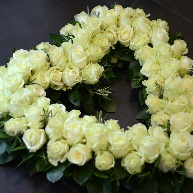 Photo showing a sample of a funeral tribute, a white rose open heart with foliage collar. White roses arranged en masse available from Kensington flowers London